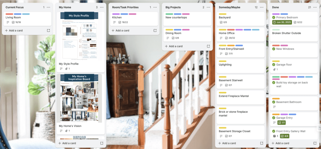 An Organize digital project management board with columns for tasks like Living Room and Kitchen, shown over a photo of a staircase with wooden railings.