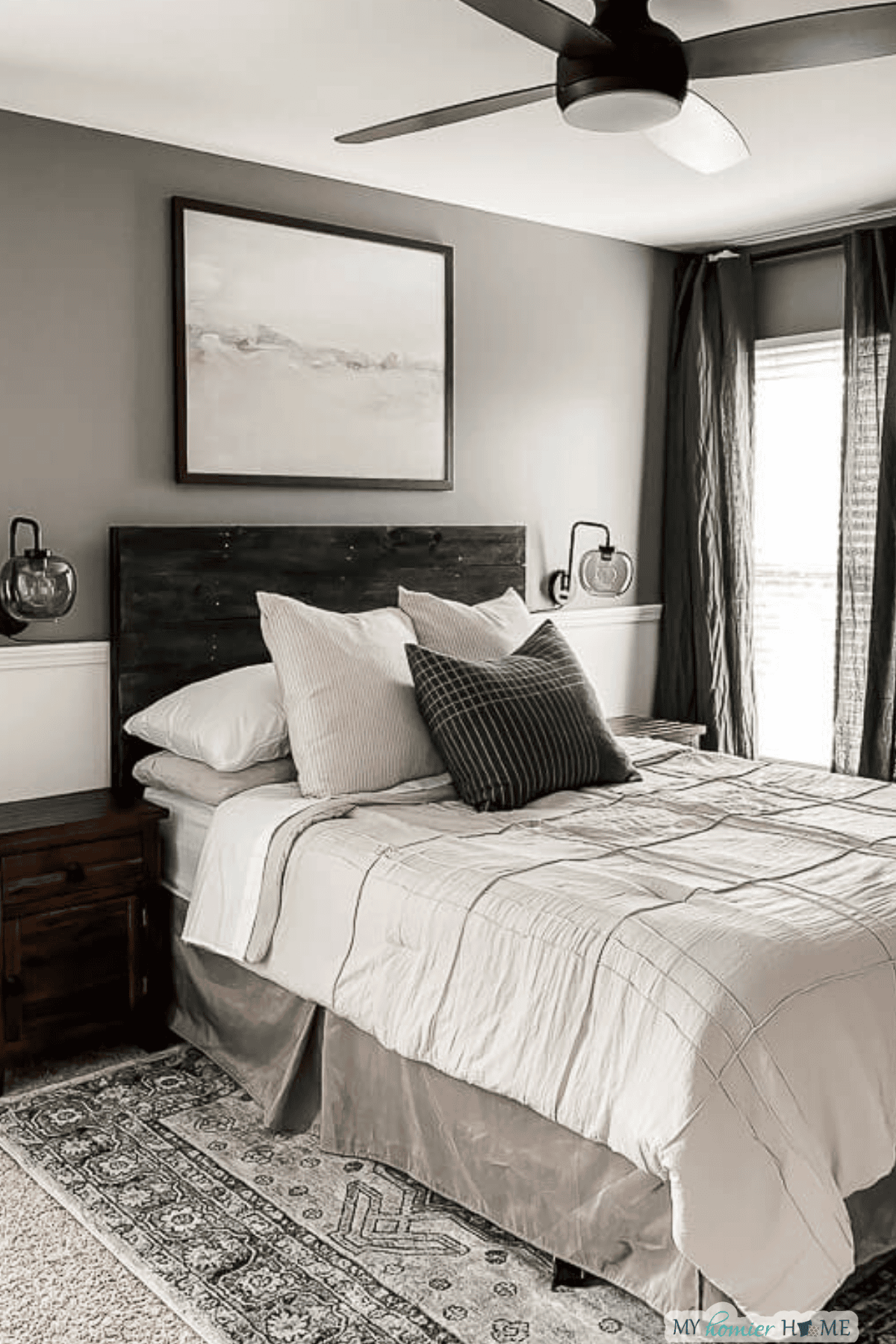 A neatly made bed with neutral bedding, dark wooden headboard, and modern ceiling fan showcases a stylish Room Refresh, complemented by abstract art and smart Small Room Design in this gray-toned bedroom.